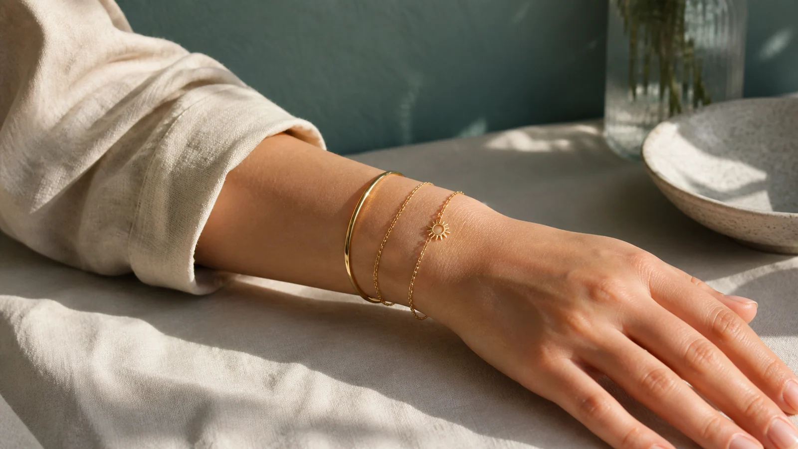 Woman stacking a sunshine charm bracelet with a fine chain and slim bangle