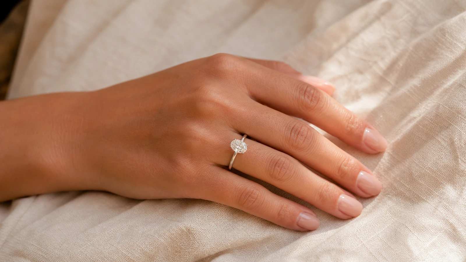 Oval moissanite engagement ring shown at a balanced scale on an adult hand