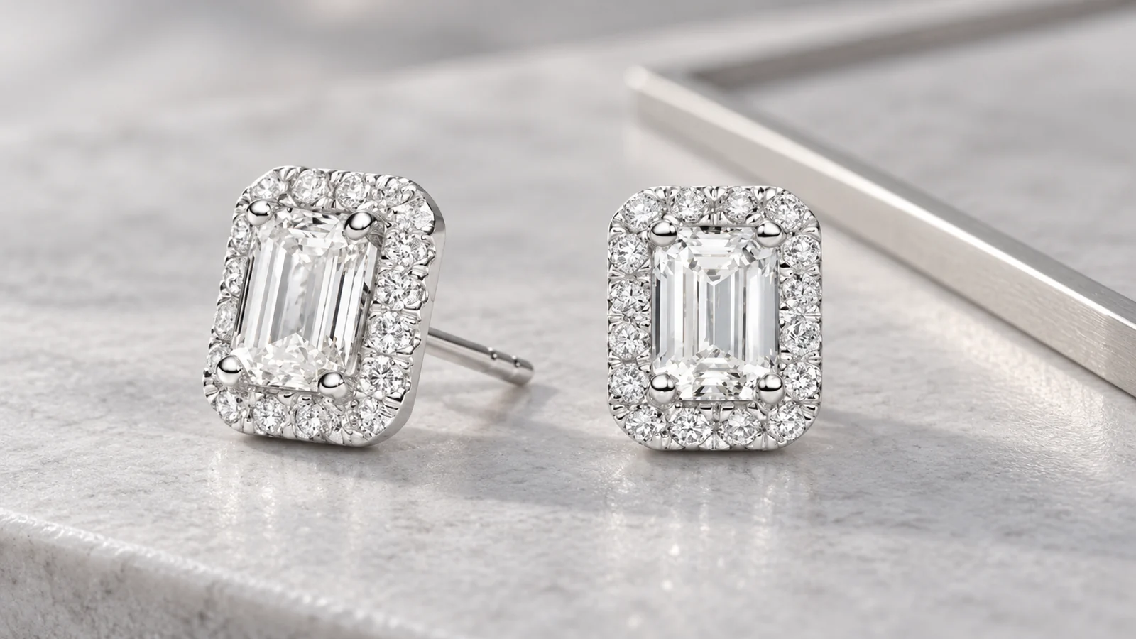 Emerald-cut halo stud earrings on pale gray stone