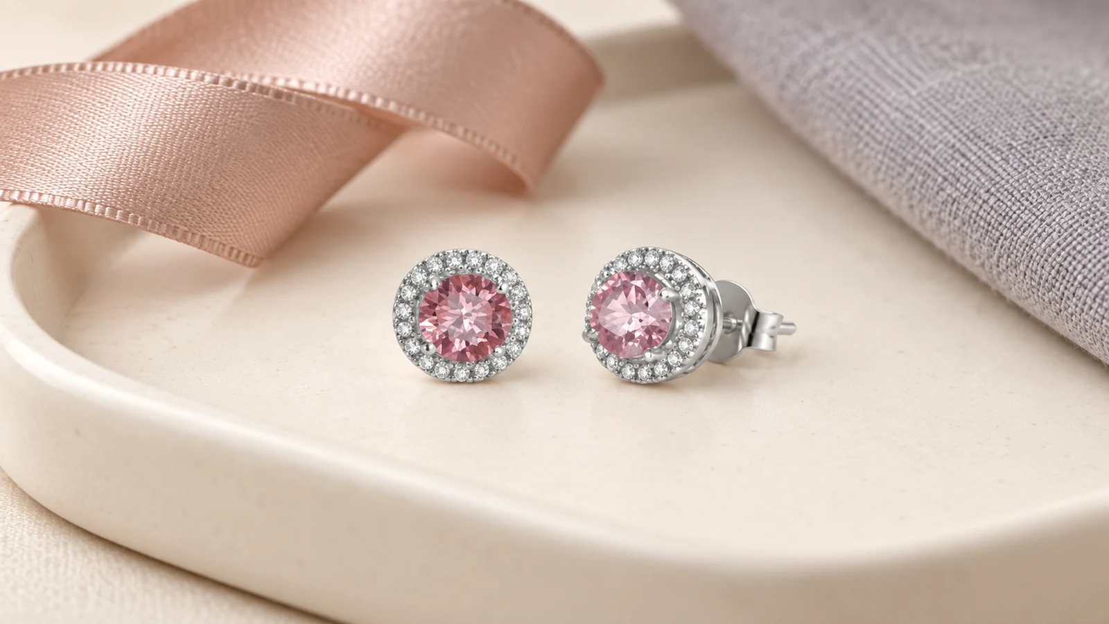 Pink halo stud earrings beside rose ribbon and gray fabric