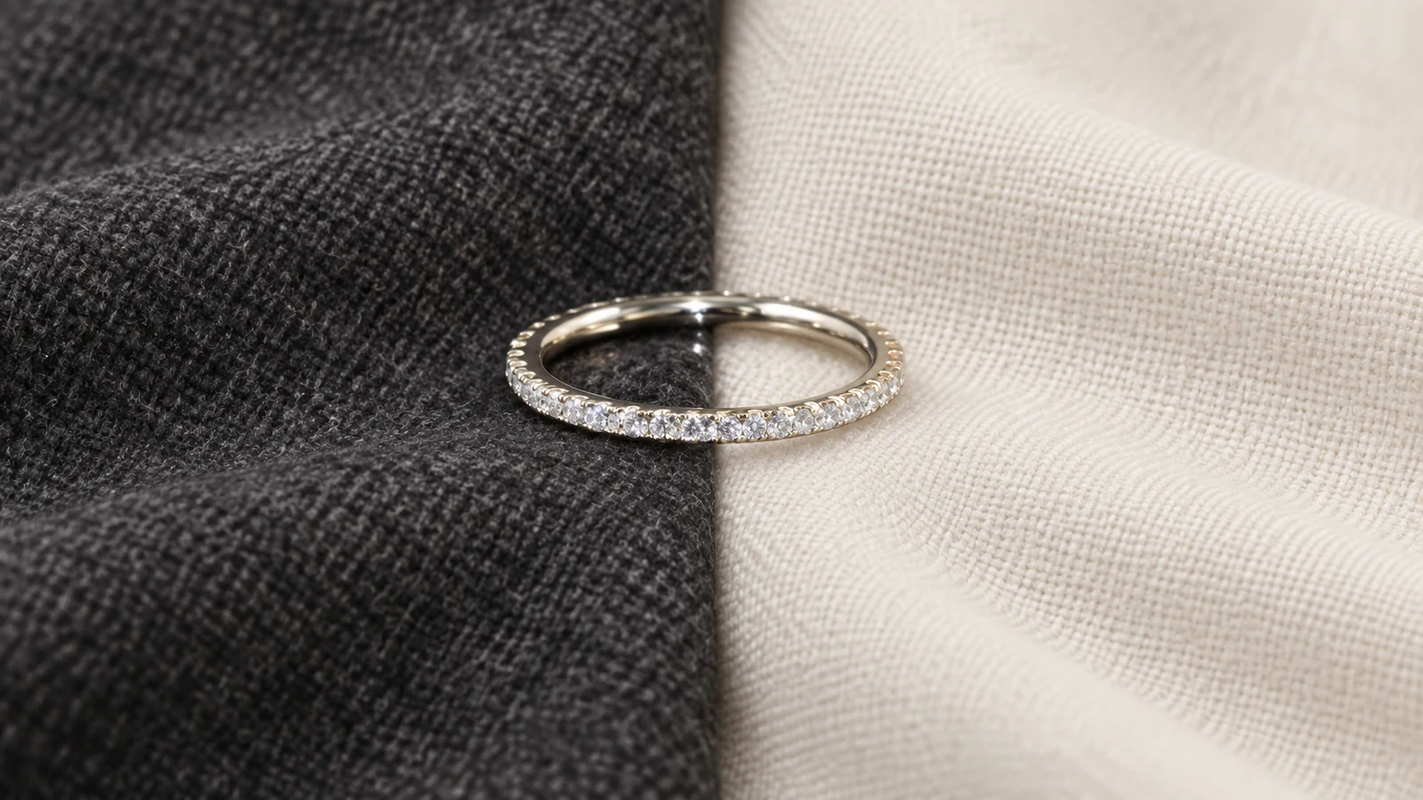 Slim white pavé eternity band across charcoal and ivory fabrics